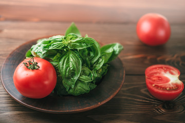 View on a brown wooden table with tomatoes and plate with green basil