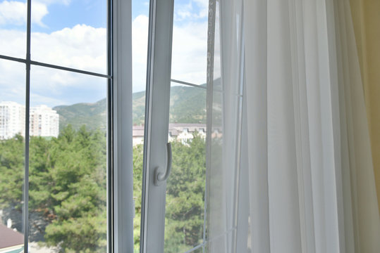 The plastic window is open. Open window with curtains and mountain views