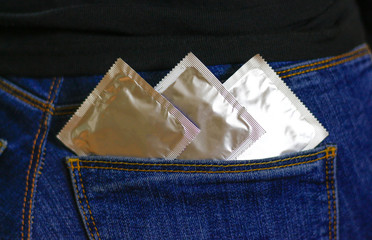 Three condoms in the pocket of blue jeans. Close up