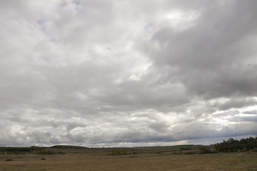 Fototapeta premium Heavy grey clouds in the cold autumn sky over fields, forests and mountains