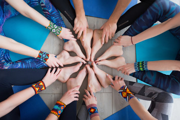 Close up of hands and legs of Group of sporty happy people sitting on the gym floor in a circle together, resting and meditating after yoga class with instructor indoors. Healthy lifestyle concept