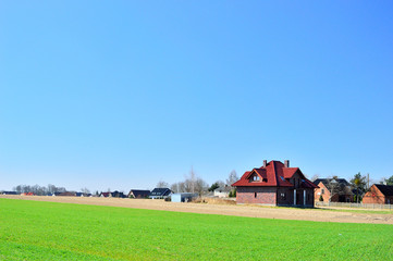Dom z czerwonym dachem na horyzoncie zielonego pola.