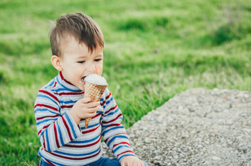 little cute boy eating ice cream three years very appetizing, amid nature, green grass