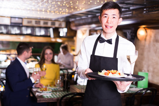 Man waiter is holding tray with wine and salad for clients