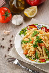 Vegetarian vegetable pasta Fusilli with tomato, parsley and olive oil in white plate on wooden table.