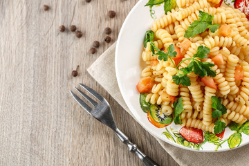 Vegetarian vegetable pasta Fusilli with tomato, parsley and olive oil in white plate on wooden table.