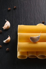 raw cannelloni pasta on black plate with spiced and garlic. Top view