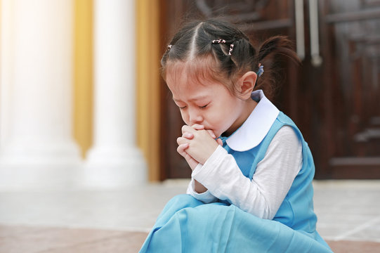 Close eyes little Asian child girl in student uniform praying. Spirituality and religion.