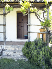 escena rural tipica de Andalucía en España de una puerta de madera en un porche con techo de tejas con hojas verdes de parra y unos escalones de acceso a la casa © tingitania
