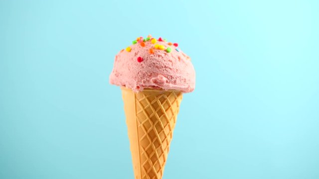 Ice cream. Strawberry or raspberry flavor icecream in waffle cone rotated over blue background. Sweet dessert decorated with colorful sprinkles closeup. 4K UHD video footage. 3840X2160