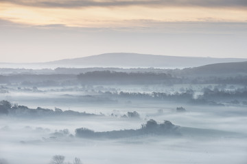 Oszałamiająco mgłowy Angielski wiejski krajobraz przy wschodem słońca w zimie z warstwami stacza się przez poly - 199771980