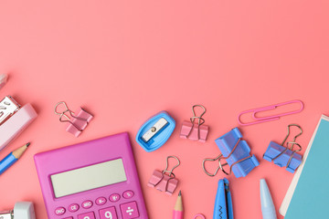 Stationary concept, Flat Lay top view Photo of Scissors, pencils, paper clips,calculator,sticky note,stapler and notepad in pink and blue tone on pink background with copy space