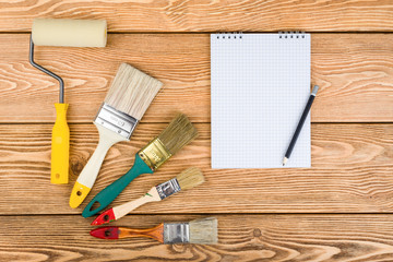 Paint brushes, roller and notepad on a wooden background 
