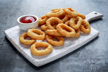 Fried Onion Rings with Ketchup on white cutting board.