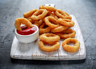 Fried Onion Rings with Ketchup on white cutting board.