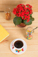 Coffee mug, red flowers, colored candy and orange peel in a jar and a yellow diary on a wooden background. breakfast or lunch