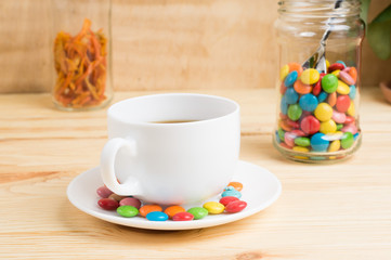 Coffee mug, colored candy and orange peel in a jar  on a wooden background. breakfast or lunch