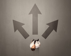 Young contemplating businessman stands in front of brown arrows