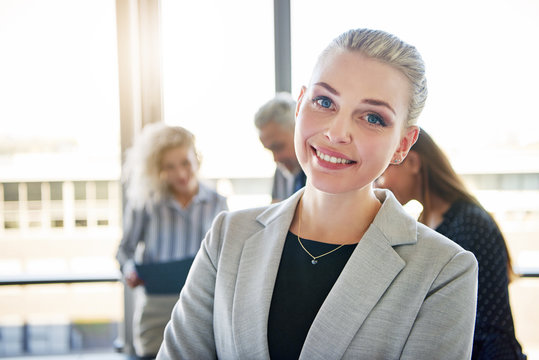Young businesswoman smiling with colleagues talking in the background