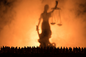 Silhouette of blurred giant lady justice statue with sword and scale standing behind crowd at night...