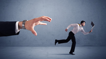 Young miniature businessman running from a big hand with blueish background
