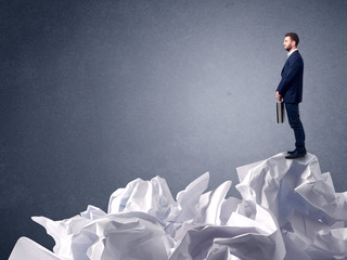 Thoughtful young businessman standing on a pile of crumpled paper 