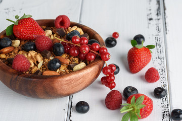Bowl of homemade granola with yogurt and fresh berries on wooden background