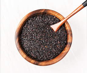 Isolated handful of raw black nero rice in the wood bowl on white background