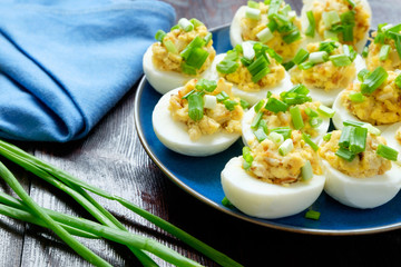 Eggs stuffed with green onion on a blue plate on a wooden background