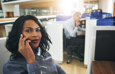 Pretty black office employee sitting and talking smartphone
