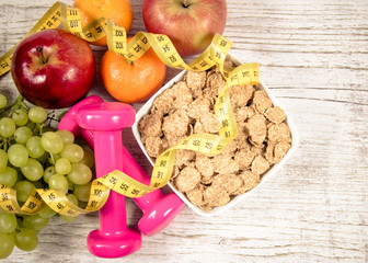 Diet fitness concept - dumbbells, measuring tape, flakes and fresh fruits on wooden table.