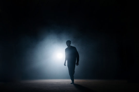 dark silhouette of slim man walking on the street at night. being alone. lighted street. thief sneaking in the street.night crime