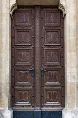 Close up view of an old, massive, wooden door deocrated with carvings and cast iron decorations and door handles 