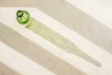 Empty green bottle on the marble surface under the natural light of the sun