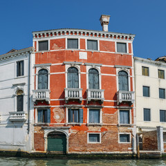 Daylight view to red historic building on a Venetian canal.