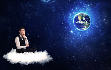 Obraz na płótnie Canvas Caucasian businessman sitting on a white fluffy cloud looking and wondering at planet earth