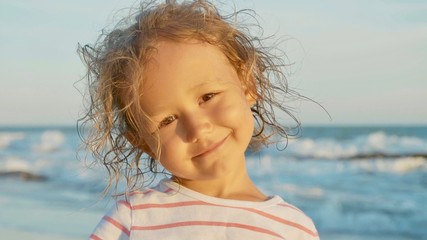 Facial portrait of beautiful little girl standing on the beach and smiling