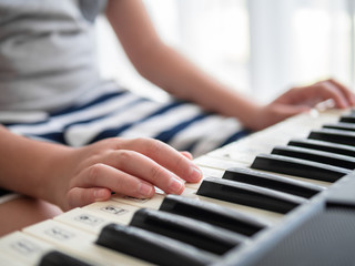 Boy playing keyboard piano near window at home.