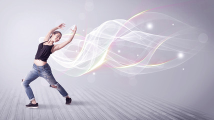Fototapeta na wymiar A beautiful young hip hop dancer dancing contemporary urban street dance in front of grey wall background with smokey lines and glitter concept.