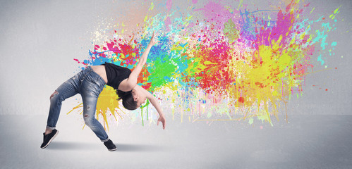 A funky contemporary hip hop dancer dancing in front of grey background with colorful bright paint splatter concept