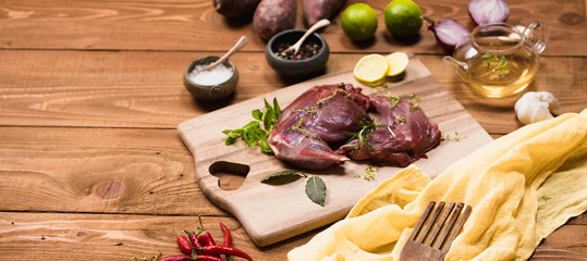 Raw rabbit legs, lime, onions, garlic, thyme and rosemary in rustic style, Sea salt, red, white pepper and coriander in clay pots on an old black rustic table. Banner, copy space
