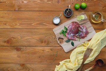 Raw rabbit legs, lime, onions, garlic, thyme and rosemary in rustic style, Sea salt, red, white pepper and coriander in clay pots on an old black rustic table. Banner, copy space, top view