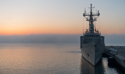 A background of a war ship in the naval base during sunset. Some navy ships in the sea with a...