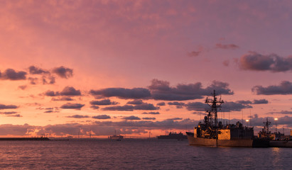 Obraz premium A background of a war ship in the naval base during sunset. Some navy ships in the sea with a marvelous orange light in the sky. 