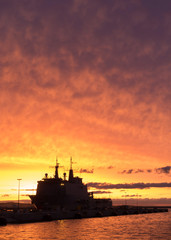 A background of a war ship in the naval base during sunset. Some navy ships in the sea with a marvelous orange light in the sky. 