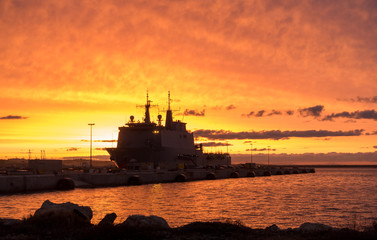 A background of a war ship in the naval base during sunset. Some navy ships in the sea with a...