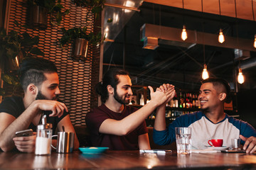 Happy arabian young man giving high five to his friend. Group of mixed race people having fun in lounge bar