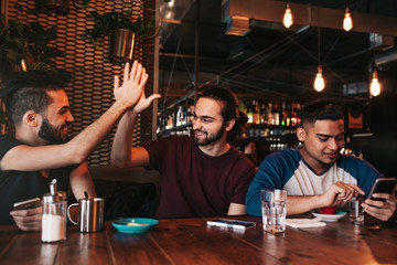 Happy arabian young man giving high five to his friend. Group of mixed race people having fun in lounge bar