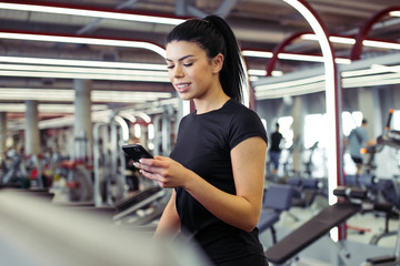 fit Sportswoman using smartphone for training workout app while jogging on treadmill