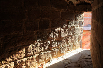stara kamienna ściana w przejściu między domami oświetlona mocnym słonecznym światłem - obrazy, fototapety, plakaty